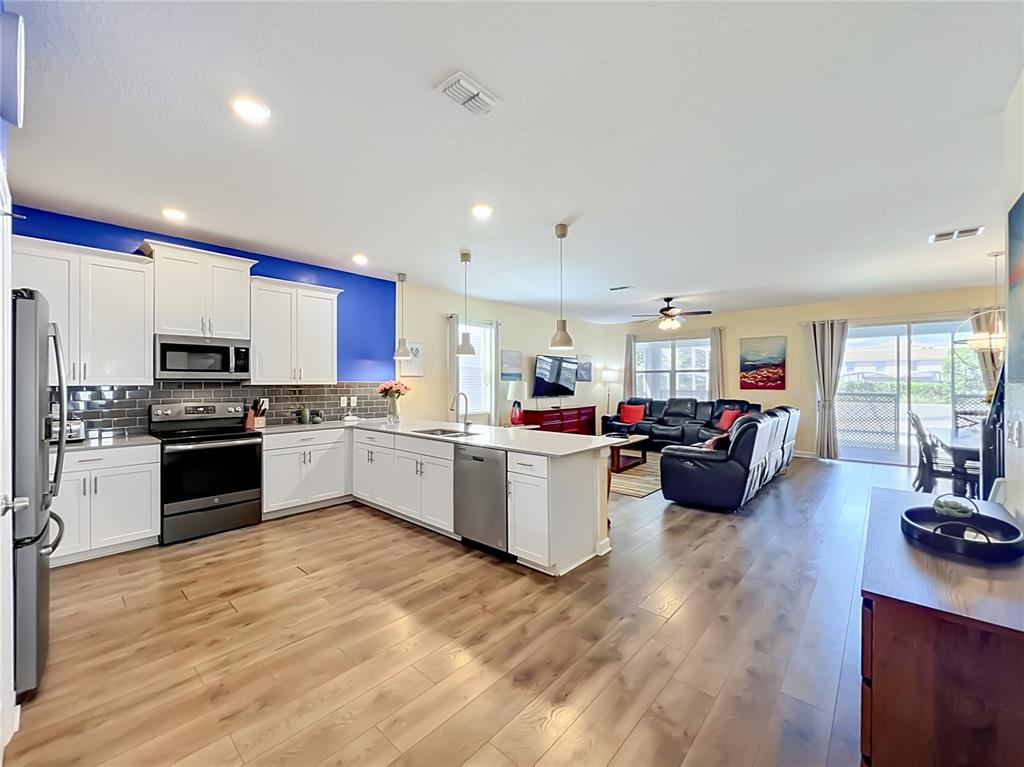 An open-concept kitchen with white cabinets and a blue accent wall overlooks a living area — 1556 MAIDSTONE COURT, DAVENPORT, FL