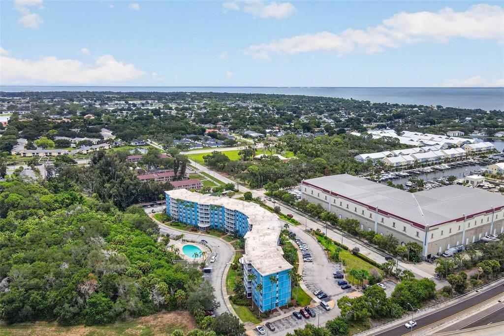 An aerial view shows a curved blue apartment building with a pool near a marina — 3315 58TH AVENUE S UNIT 105, ST PETERSBURG, FL