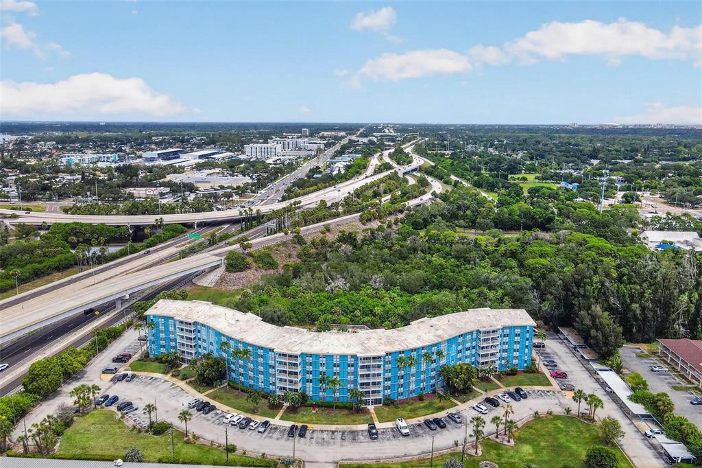 An aerial view shows a multi-story blue apartment building surrounded by parking lots and highways — 3315 58TH AVENUE S UNIT 105, ST PETERSBURG, FL