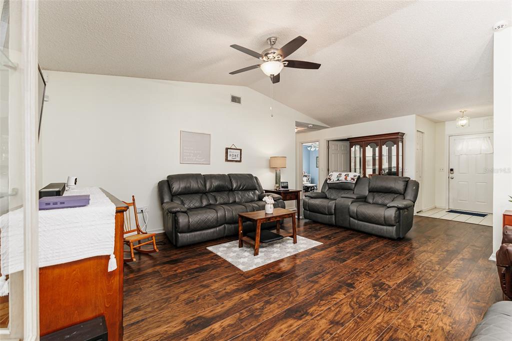 A living room features dark wood flooring, two grey leather sofas, and a ceiling fan — 1836 PRAIRIE DUNES CIRCLE N, LAKELAND, FL