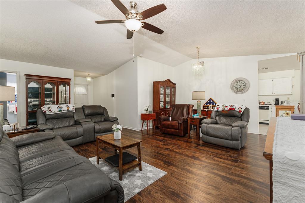 A living room features dark wood-look flooring, gray leather furniture, and a vaulted ceiling — 1836 PRAIRIE DUNES CIRCLE N, LAKELAND, FL