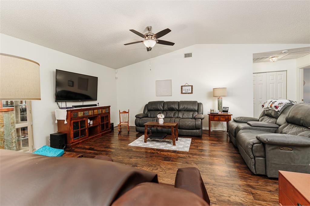 A living room features dark wood flooring, a vaulted ceiling, and two leather sofas — 1836 PRAIRIE DUNES CIRCLE N, LAKELAND, FL