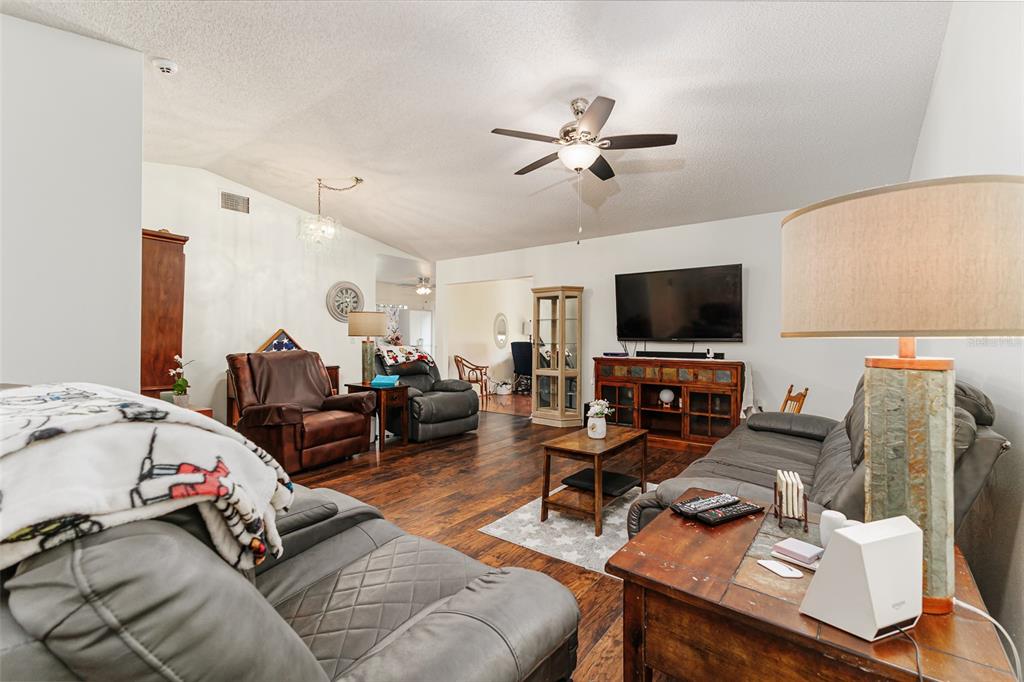 A living room features dark wood flooring, a ceiling fan, and gray leather furniture — 1836 PRAIRIE DUNES CIRCLE N, LAKELAND, FL