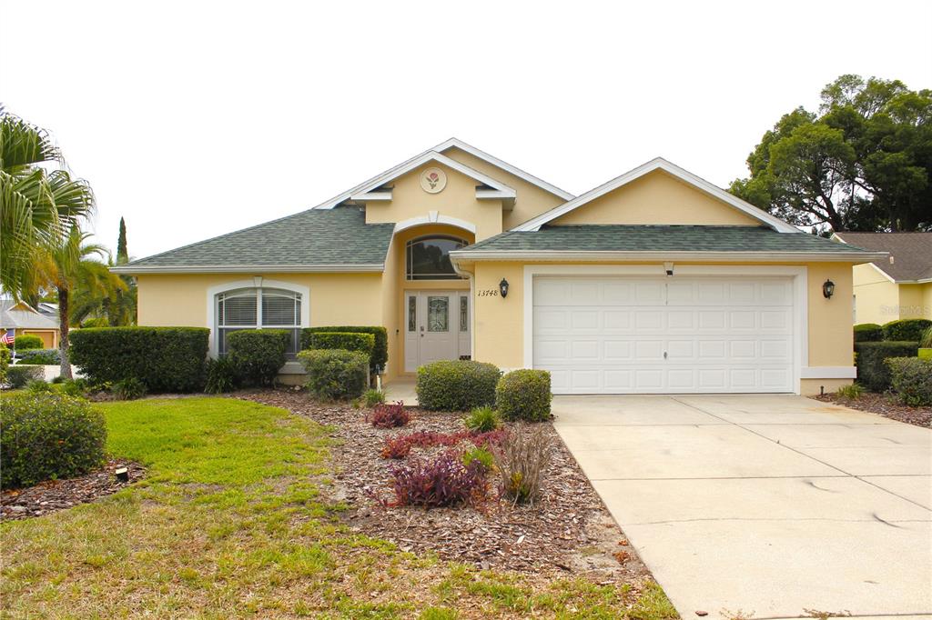 A single-story house with a yellow stucco exterior, a green shingled roof, and a two-car garage — 13748 MEADE COURT, HUDSON, FL