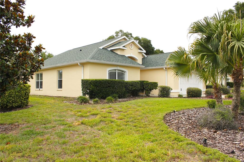 A single-story house with a yellow stucco exterior, green shingled roof, and a palm tree — 13748 MEADE COURT, HUDSON, FL