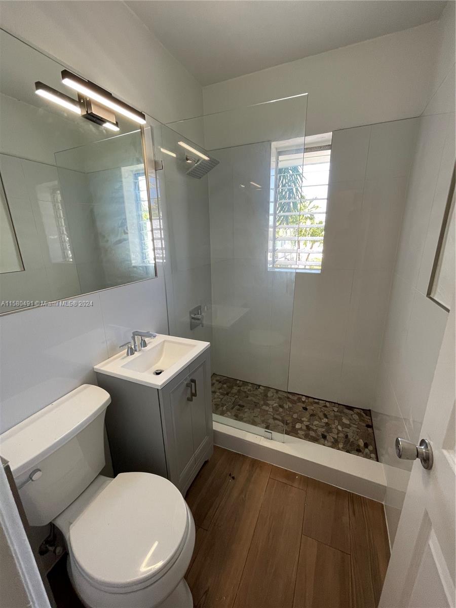 A small bathroom features a glass-enclosed shower with pebble flooring, a vanity, and wood-look tile — 760 Jefferson Ave # 11, Miami Beach FL 33139, MIAMI BEACH, FL