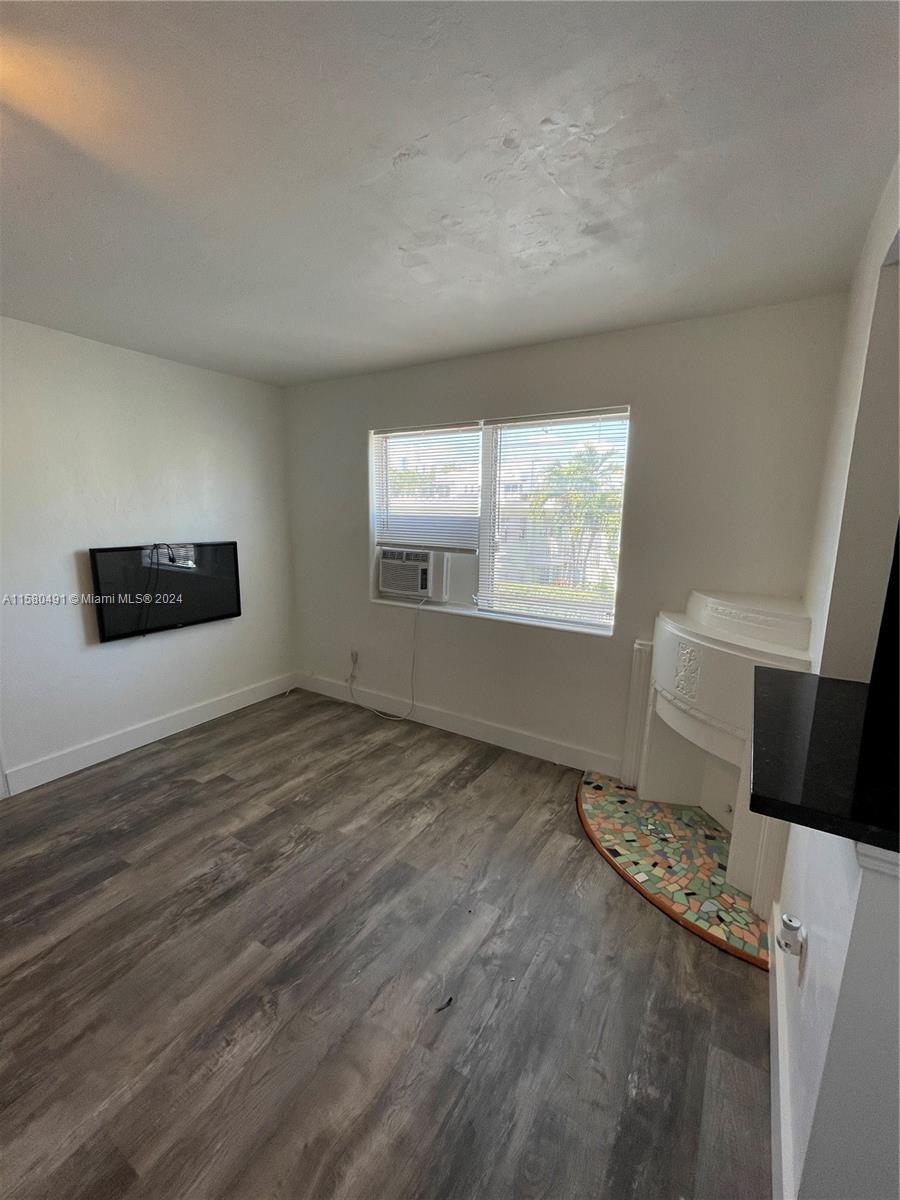 A room with wood-look flooring, a wall-mounted television, a window air conditioner, and a fireplace — 760 Jefferson Ave # 11, Miami Beach FL 33139, MIAMI BEACH, FL