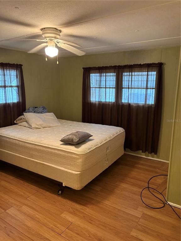 A bedroom features a bed with white bedding, wood-look flooring, and brown curtains over windows — 6580 SEMINOLE UNIT 102, SEMINOLE, FL