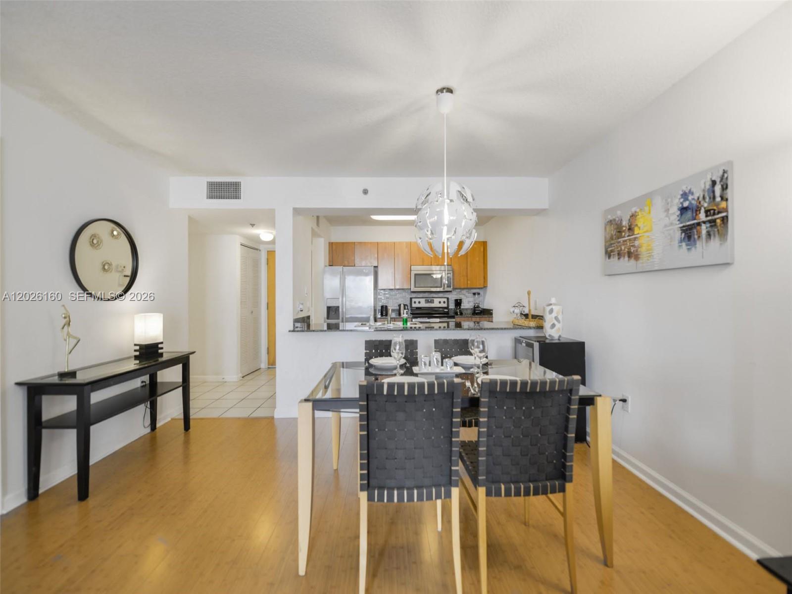 A dining area with a glass table and woven chairs sits before an open kitchen — 1200 Brickell Bay Dr # 2119, Miami FL 33131, MIAMI, FL