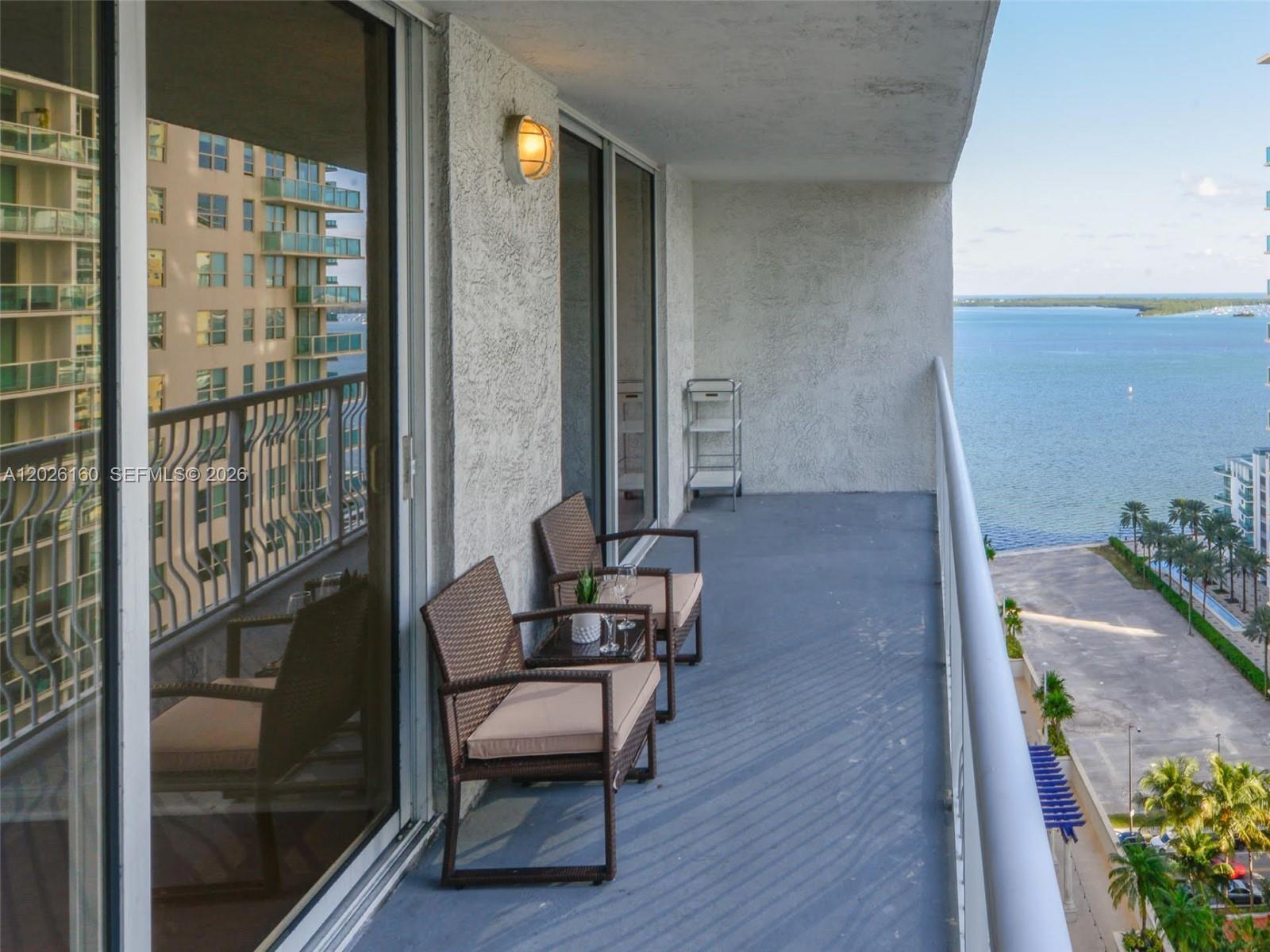 A balcony with two wicker chairs, a small table, and a view of the ocean — 1200 Brickell Bay Dr # 2119, Miami FL 33131, MIAMI, FL
