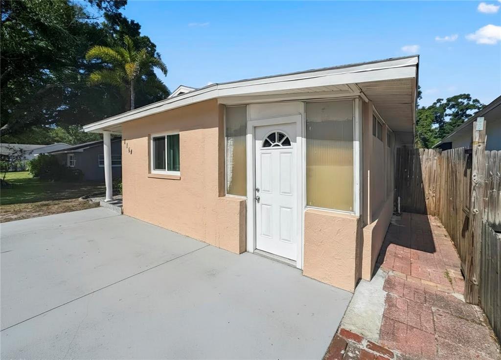 A tan stucco house exterior features a white front door, side windows, and concrete driveway — 7154 63RD STREET N, PINELLAS PARK, FL