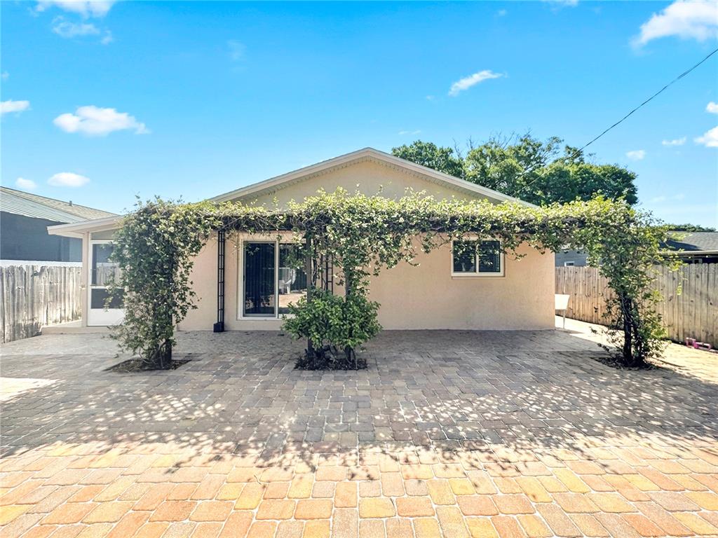 A beige house exterior features a large brick paver patio covered by a vine-covered pergola — 7154 63RD STREET N, PINELLAS PARK, FL