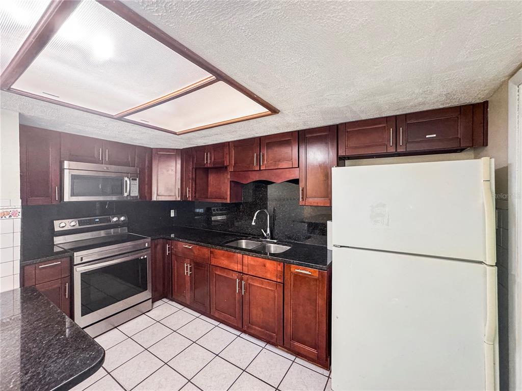 A kitchen features dark wood cabinets, black granite countertops, stainless steel appliances, and white tile flooring — 7154 63RD STREET N, PINELLAS PARK, FL