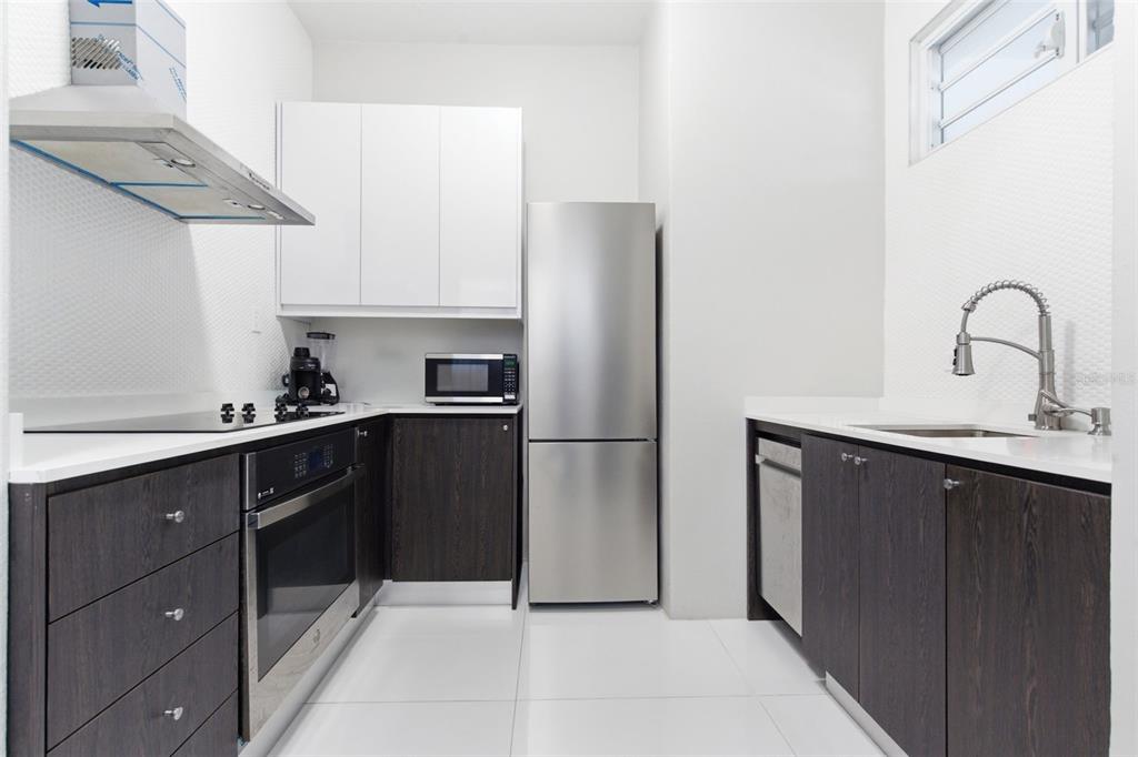 A modern kitchen features dark wood lower cabinets, white upper cabinets, and stainless steel appliances — 56 CALLE F KRUG CONDADO UNIT 1, SAN JUAN, PR