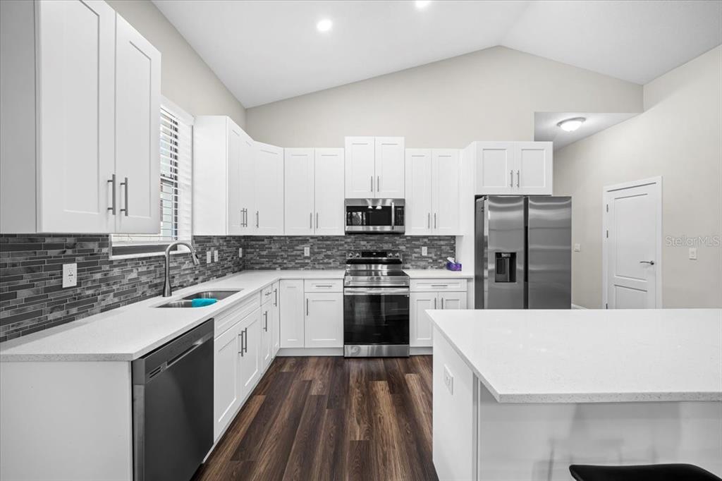 A modern kitchen features white cabinets, stainless steel appliances, a tiled backsplash, and wood flooring — 11 GREEN CIRCLE, PALM COAST, FL