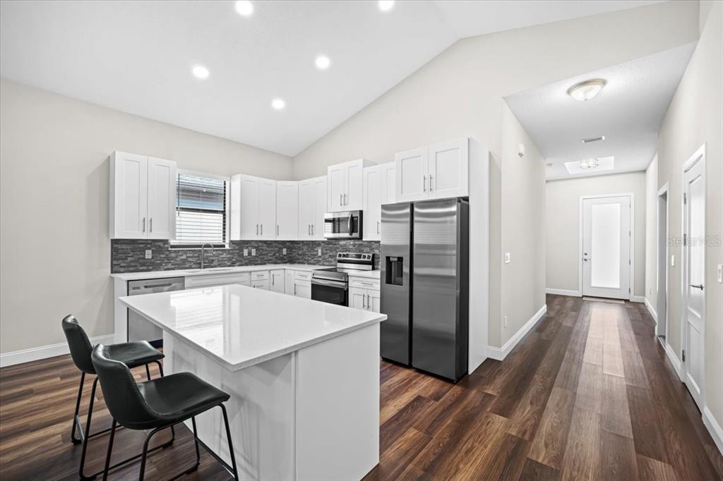A modern kitchen features white cabinets, stainless steel appliances, a quartz island, and wood flooring — 11 GREEN CIRCLE, PALM COAST, FL