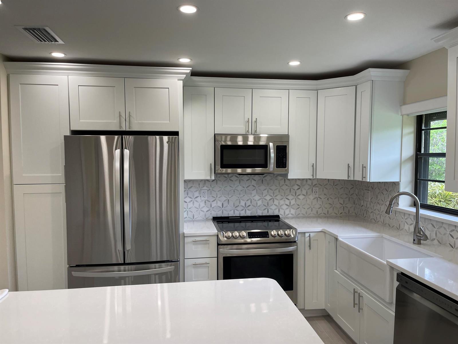 A modern kitchen features white cabinetry, stainless steel appliances, a farmhouse sink, and patterned backsplash — 29 Bethesda Park Circle # G29, Boynton Beach FL 33435, BOYNTON BEACH, FL