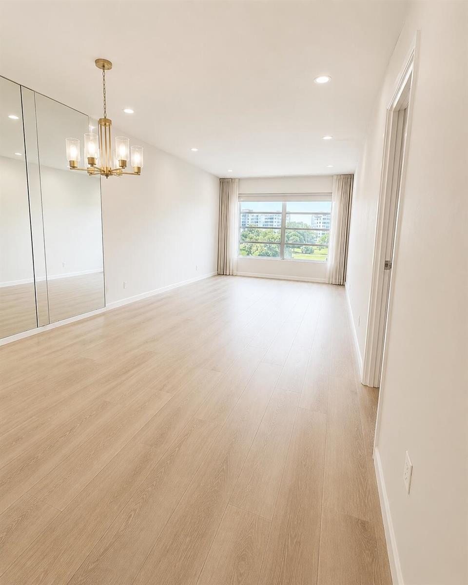 An empty room with light wood flooring, a gold chandelier, mirrored closet doors, and windows — 2900 N Palm Aire Drive # 307, Pompano Beach FL 33069, POMPANO BEACH, FL