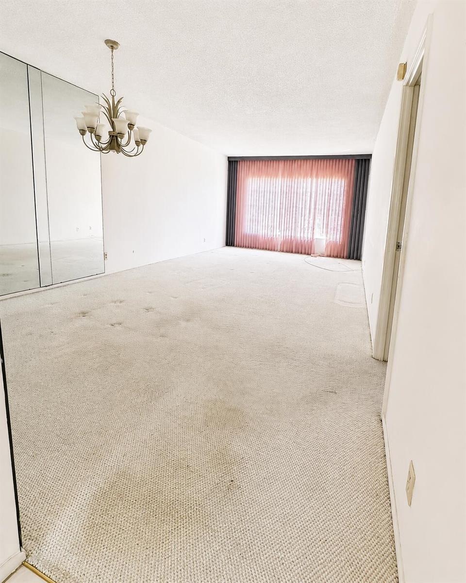 An empty room features beige wall-to-wall carpeting, mirrored closet doors, and a hanging chandelier — 2900 N Palm Aire Drive # 307, Pompano Beach FL 33069, POMPANO BEACH, FL