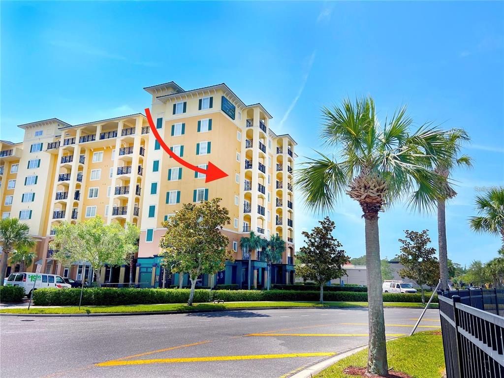 A multi-story yellow apartment building stands behind a palm tree and a paved road — 8112 POINCIANA BOULEVARD UNIT 1502, ORLANDO, FL