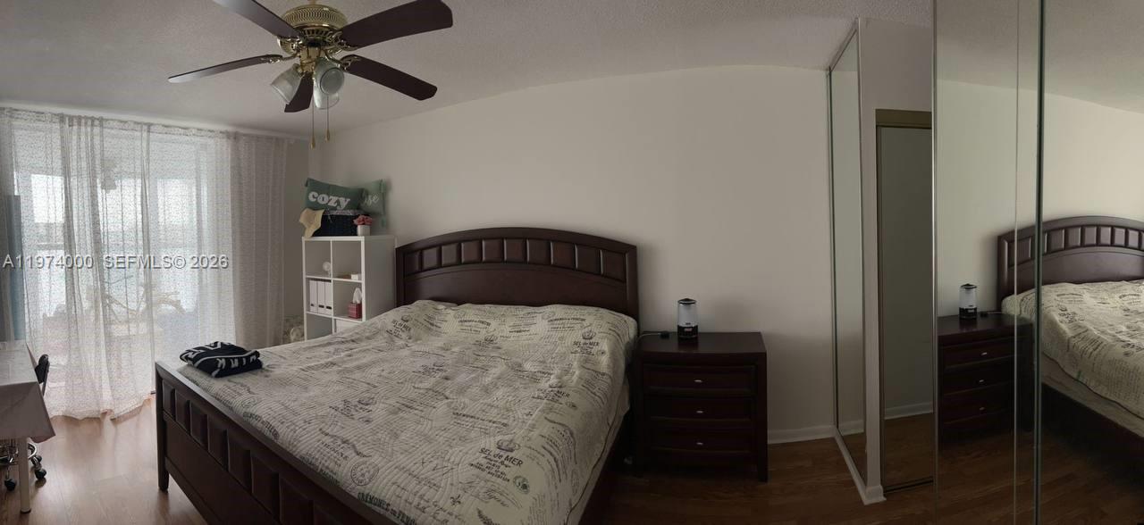 A bedroom features a wooden bed frame, a nightstand, and mirrored closet doors — 1150 NE 191st St # 34, Miami FL 33179, MIAMI, FL