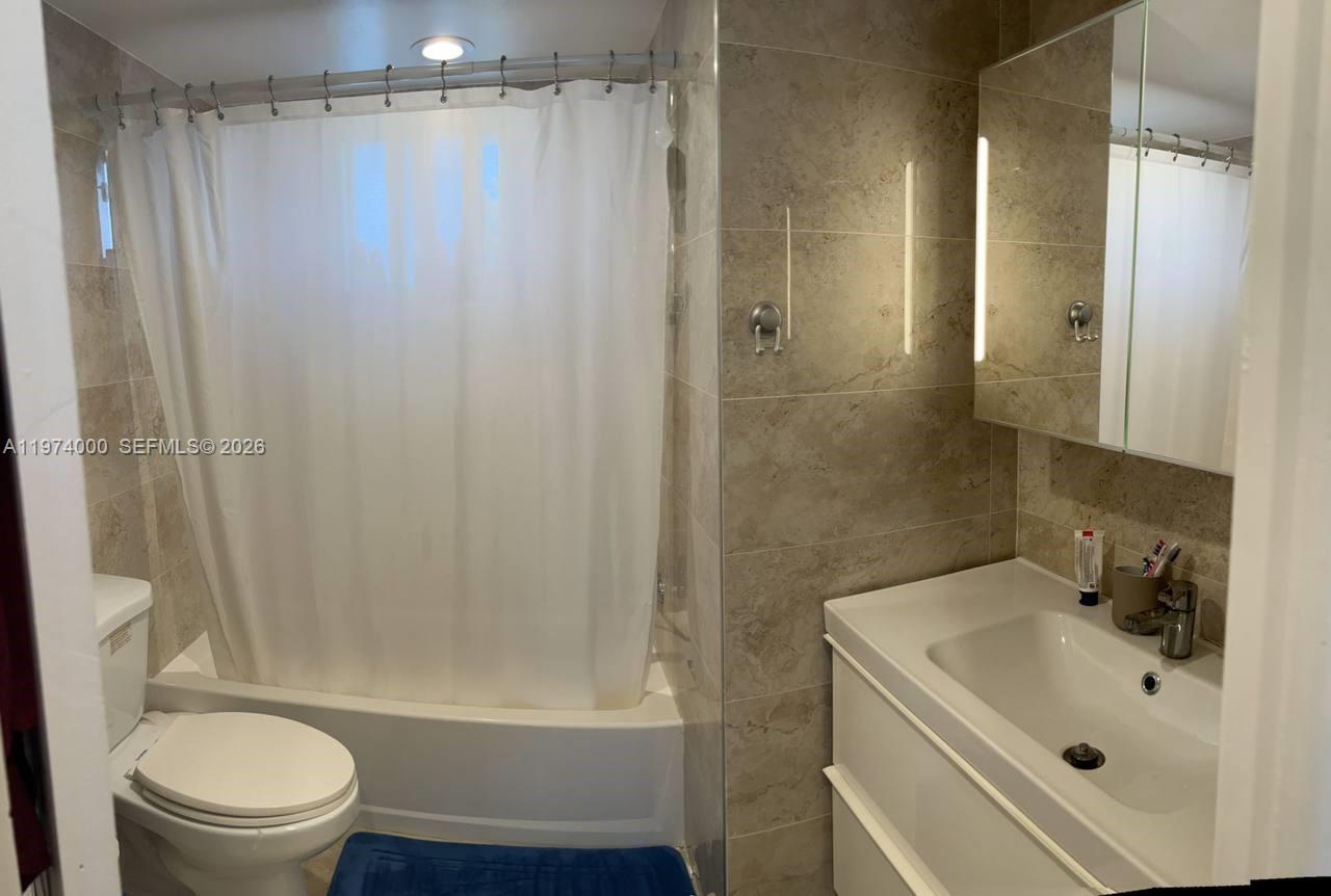 A bathroom features a white toilet, a bathtub with a shower curtain, and a vanity — 1150 NE 191st St # 34, Miami FL 33179, MIAMI, FL