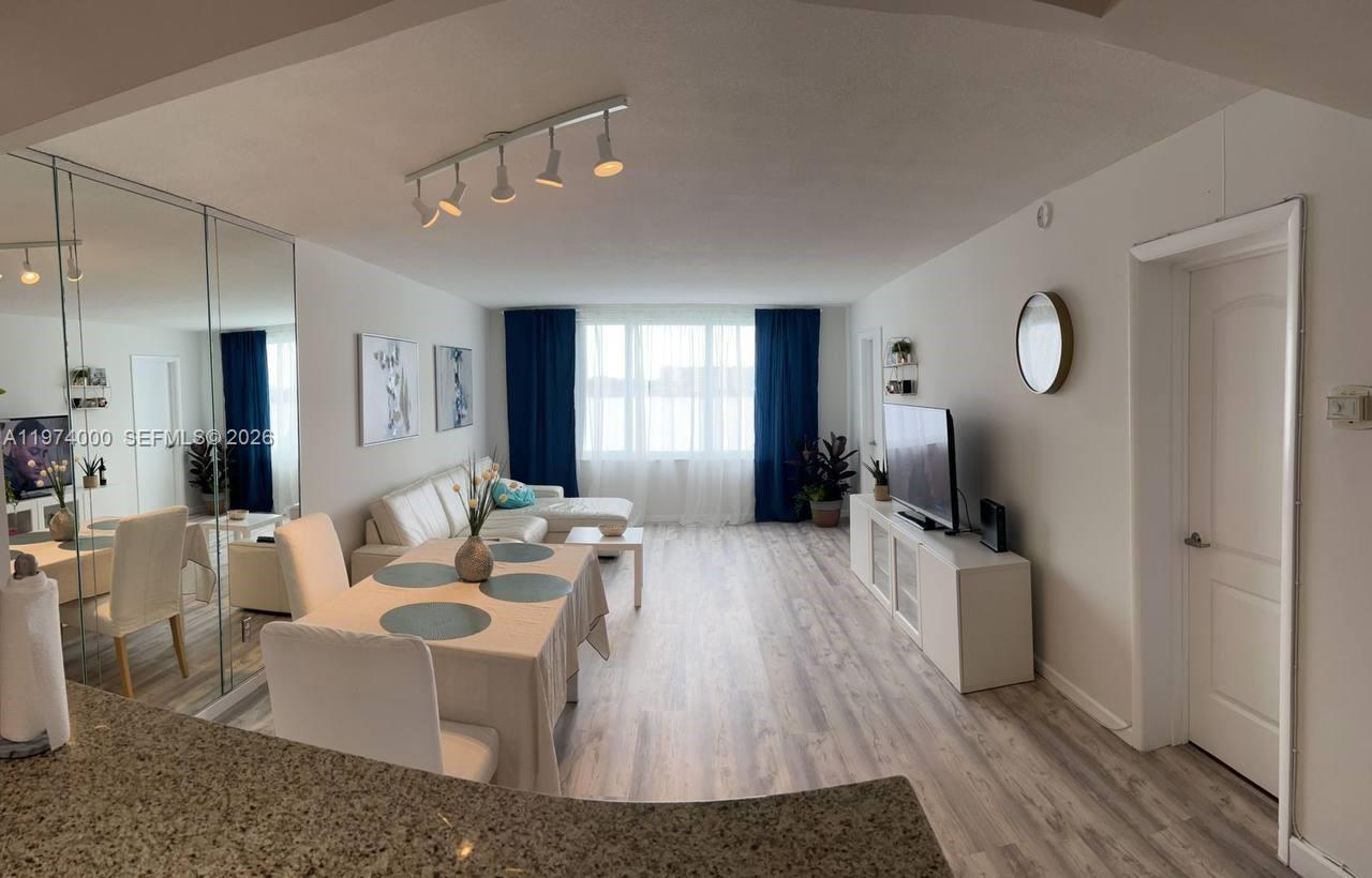 A living and dining area features light wood-look flooring, white furniture, and dark blue curtains — 1150 NE 191st St # 34, Miami FL 33179, MIAMI, FL