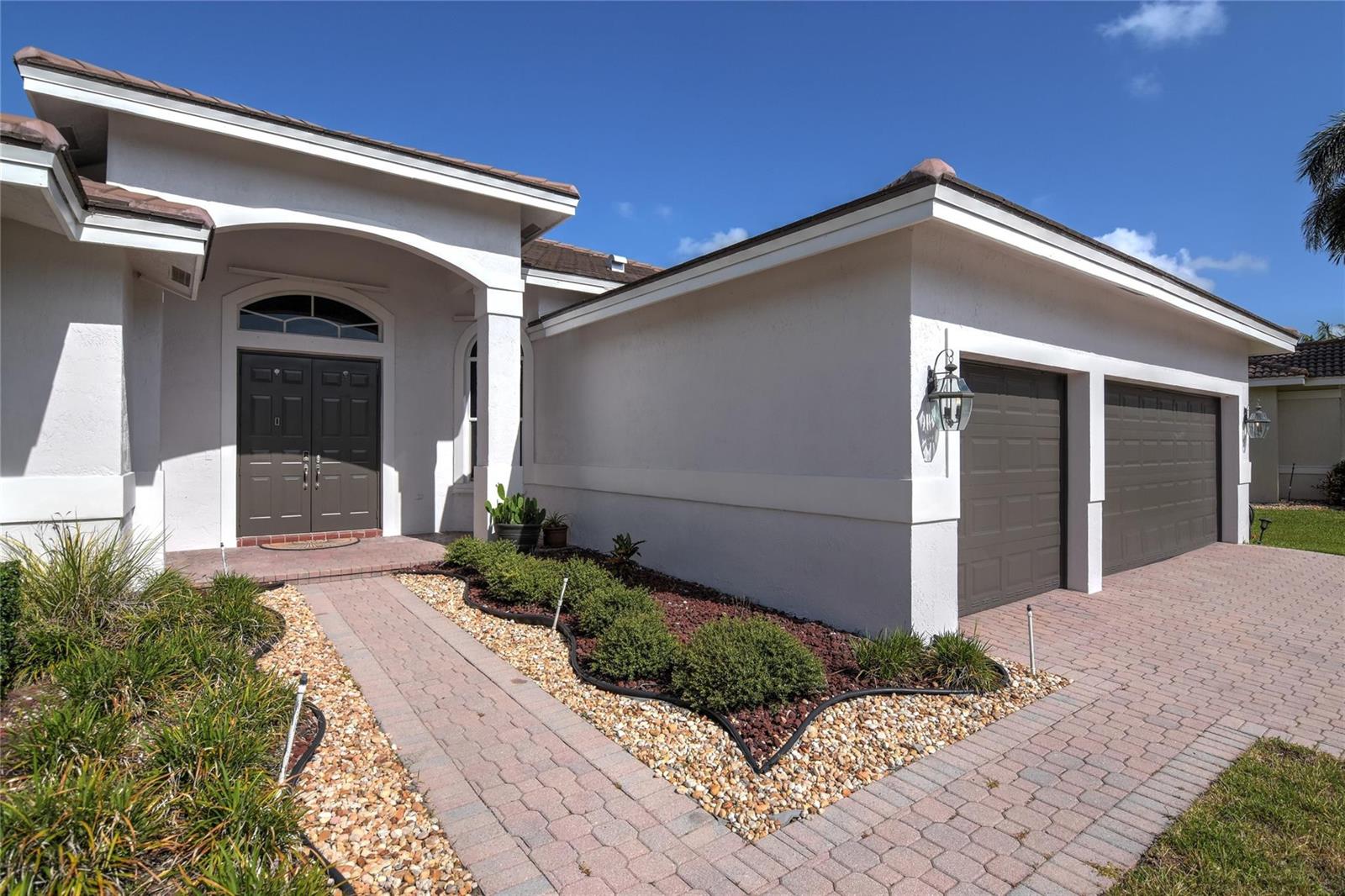 A single-story house exterior features a paved walkway, a landscaped garden, and a two-car garage — 1125 Waterside Circle, Weston FL 33327, WESTON, FL
