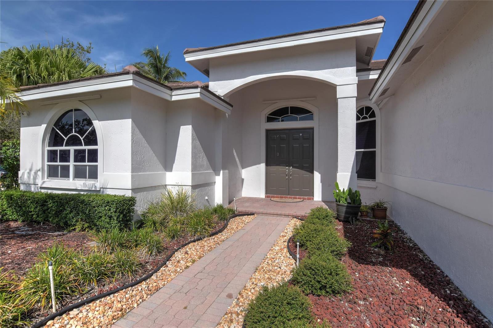 A white stucco house features a brick walkway leading to a dark double front door — 1125 Waterside Circle, Weston FL 33327, WESTON, FL