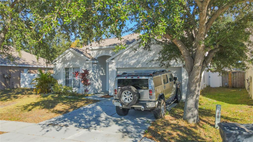 A tan single-story house with a driveway and a parked SUV under a large tree — 10606 WALKER VISTA DRIVE, RIVERVIEW, FL