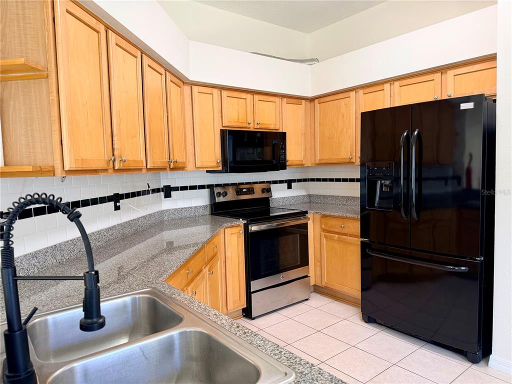 A kitchen features light wood cabinets, granite countertops, a black refrigerator, and a stainless stove — 7838 CARRIAGE POINTE DRIVE, GIBSONTON, FL