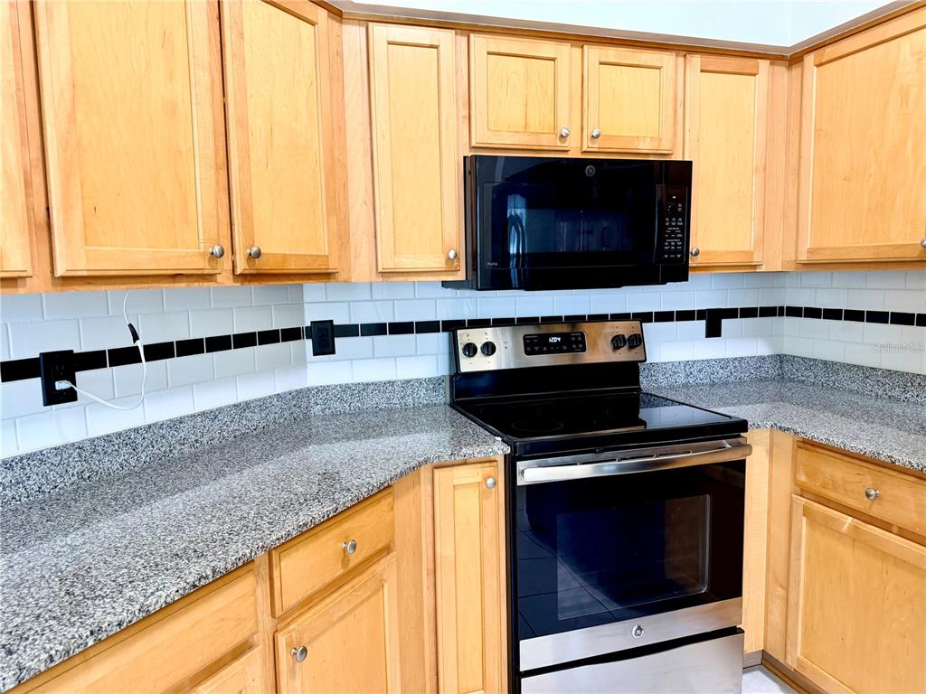 A kitchen features light wood cabinets, granite countertops, a black microwave, and a stainless stove — 7838 CARRIAGE POINTE DRIVE, GIBSONTON, FL