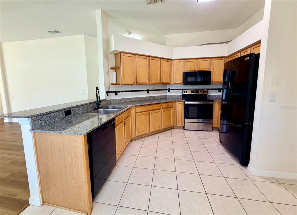 A kitchen features light wood cabinets, granite countertops, black appliances, and tiled flooring — 7838 CARRIAGE POINTE DRIVE, GIBSONTON, FL