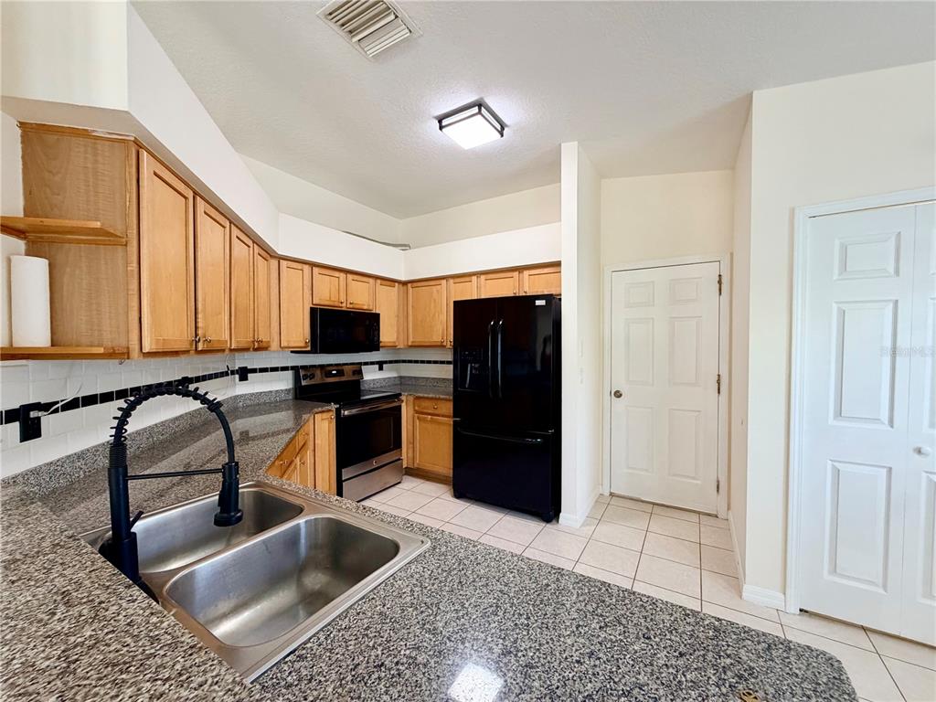 A kitchen features light wood cabinets, granite countertops, a black refrigerator, and a double sink — 7838 CARRIAGE POINTE DRIVE, GIBSONTON, FL