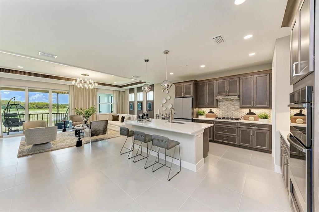 An open-concept kitchen and living area features dark wood cabinetry, a quartz island, and patio — 10016 REMBRANDT WAY UNIT 201, BRADENTON, FL