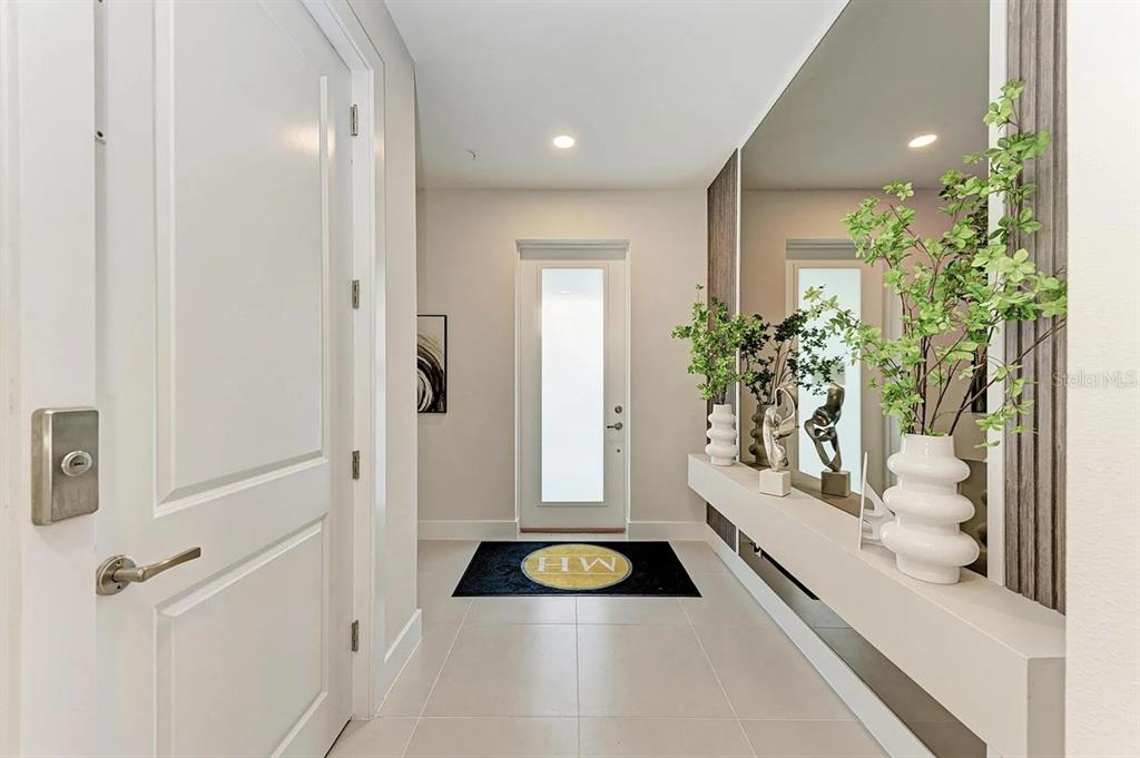 A bright entryway features a white door, a floating console table, and a large mirror — 10016 REMBRANDT WAY UNIT 201, BRADENTON, FL