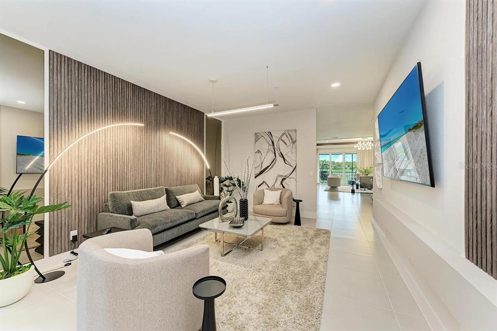 A modern living room features a slatted wood accent wall, arched floor lamp, and television — 10016 REMBRANDT WAY UNIT 201, BRADENTON, FL