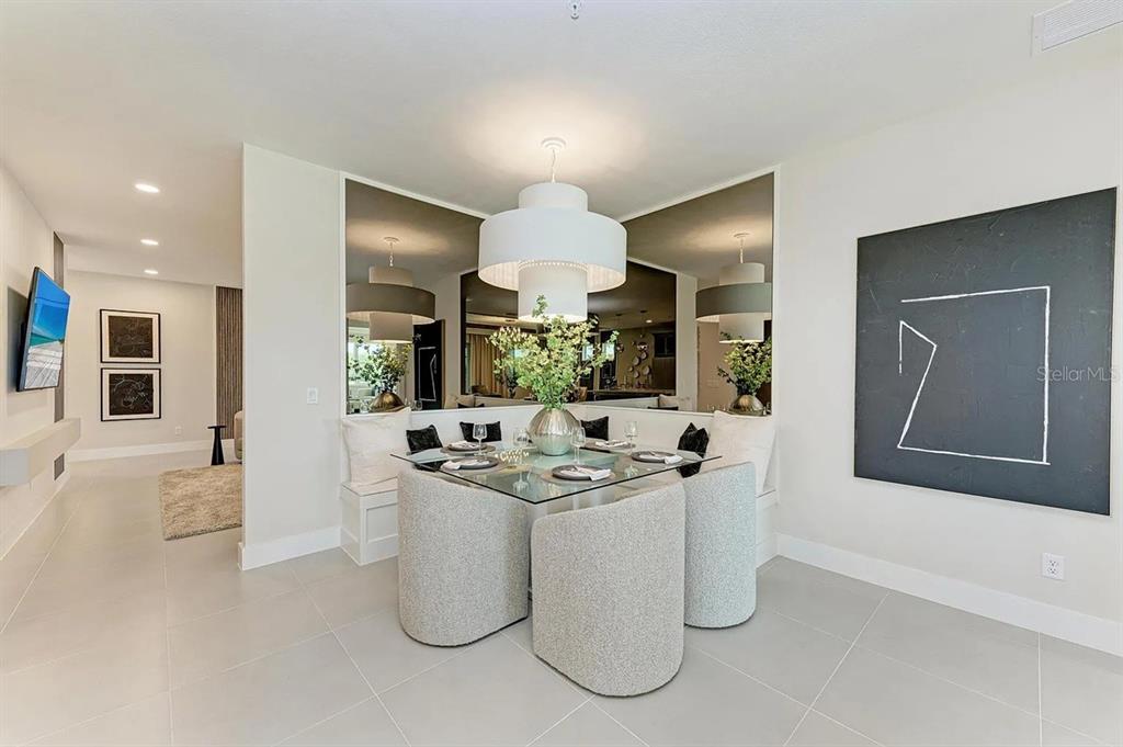 A dining area features a glass table, three upholstered chairs, a built-in bench, and mirrors — 10016 REMBRANDT WAY UNIT 201, BRADENTON, FL