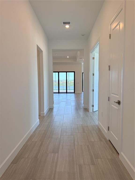 A hallway with light wood-look tile flooring leads toward a room with large sliding glass doors — 4821 LONG POINT RUN, LAKEWOOD RANCH, FL