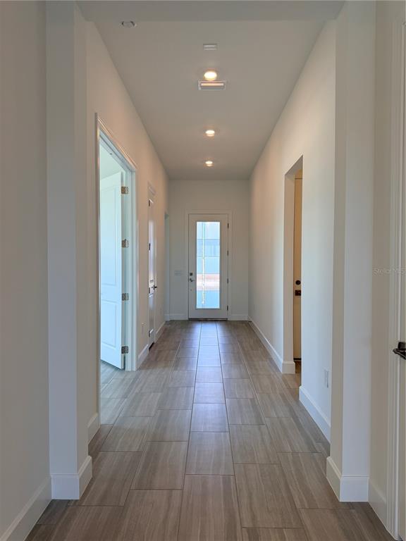 A hallway with light wood-look tile flooring leads to a glass-paneled front door — 4821 LONG POINT RUN, LAKEWOOD RANCH, FL