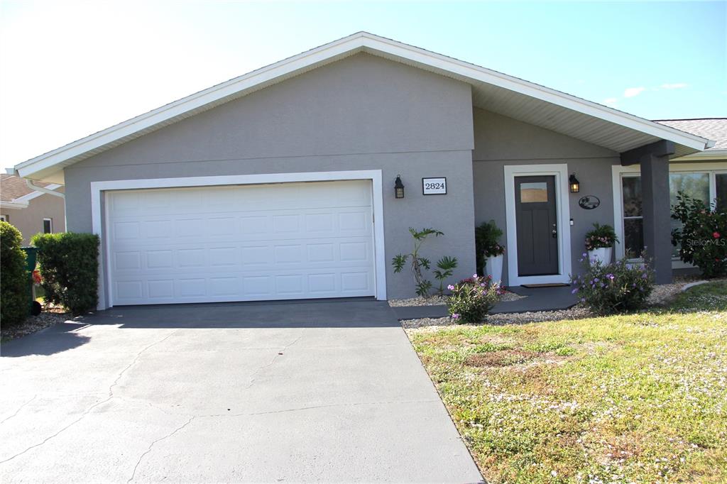 A gray single-story house features a white garage door, a dark front door, and landscaping — 2824 SHANNON DRIVE, PUNTA GORDA, FL