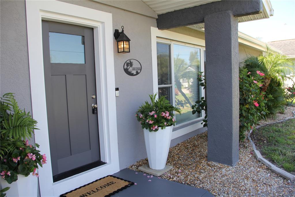 A gray front door with a glass panel is set in a light gray exterior wall — 2824 SHANNON DRIVE, PUNTA GORDA, FL