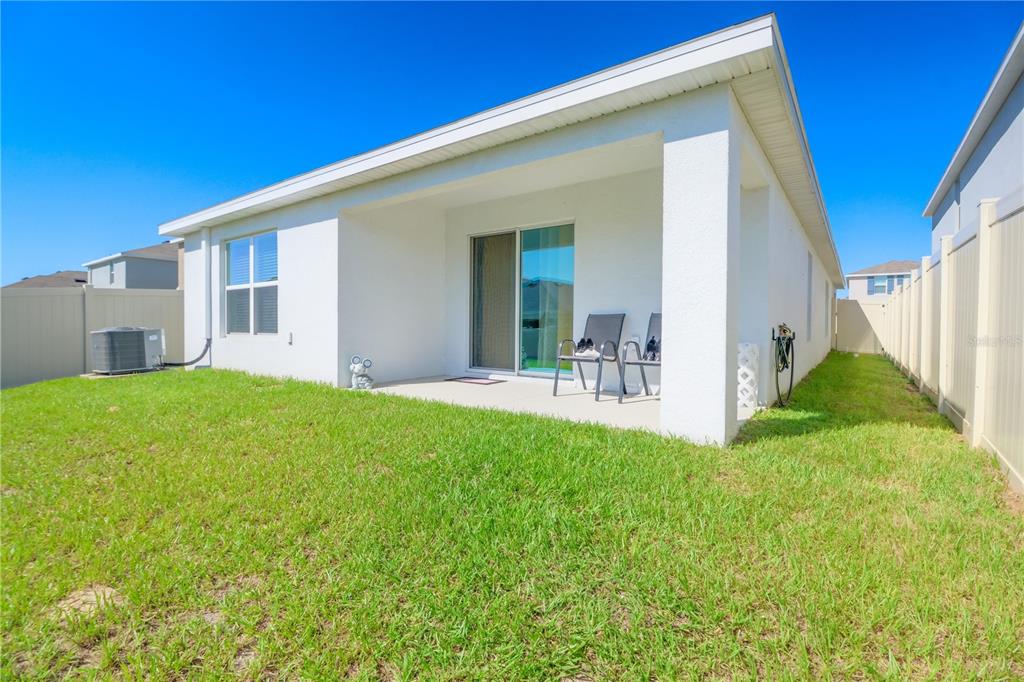 A white stucco house features a covered concrete patio and a fenced backyard — 8695 SW 46TH AVENUE, OCALA, FL