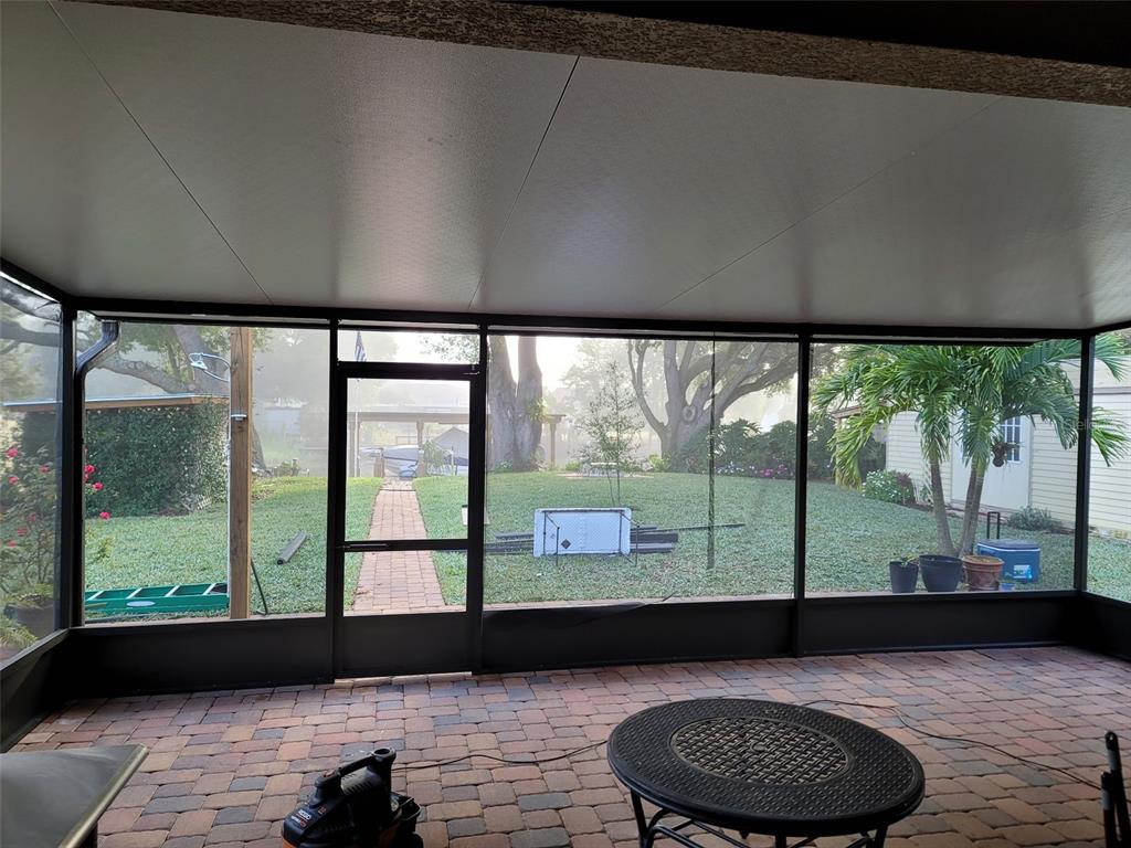 A screened-in patio with brick flooring overlooks a backyard with a brick walkway and trees — 27728 LISA DRIVE, TAVARES, FL