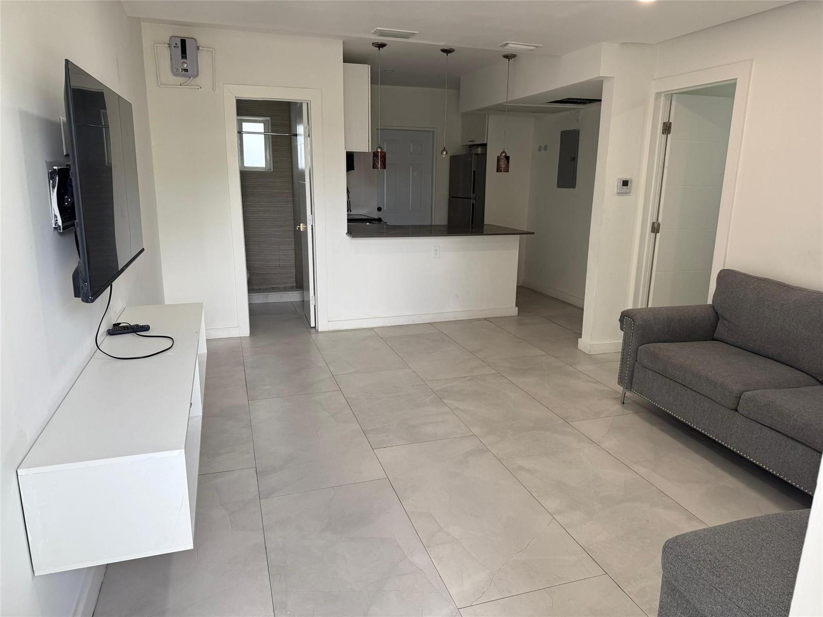 A living room with gray tile floors, a wall-mounted television, and an open kitchen — 2201 Greene Street # 1, Hollywood FL 33020, HOLLYWOOD, FL