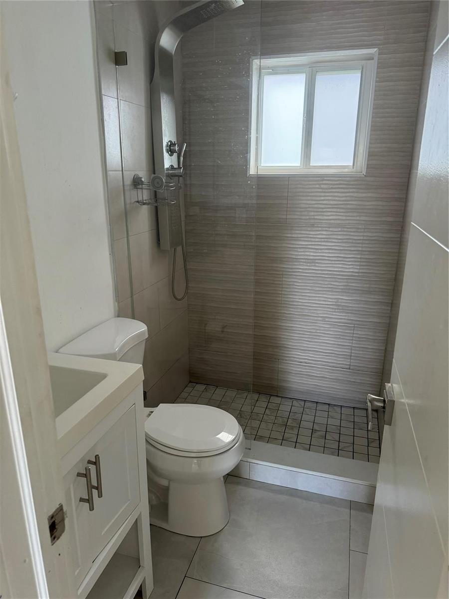 A small bathroom features a white vanity, a toilet, and a walk-in shower with tile — 2201 Greene Street # 1, Hollywood FL 33020, HOLLYWOOD, FL