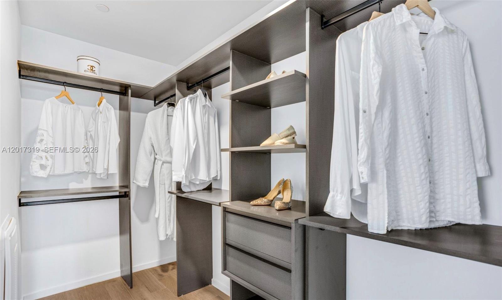 A walk-in closet features dark wood shelving, hanging white clothing, and a Chanel hat box — 398 NE 5th St # 4701, Miami FL 33132, MIAMI, FL