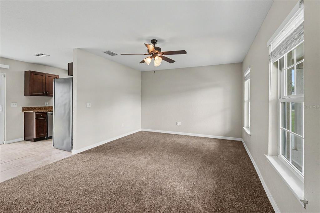 A carpeted living room with a ceiling fan and an adjacent kitchen with brown cabinets — 14945 SW 39TH CIRCLE, OCALA, FL