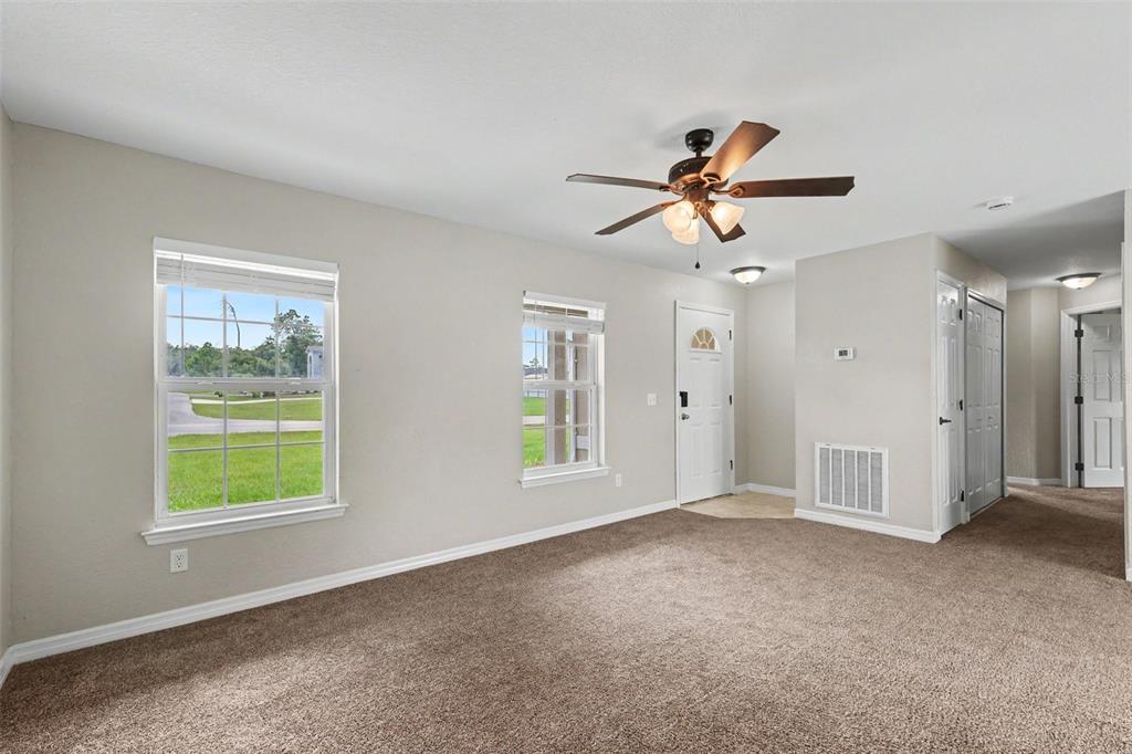 An empty living room with beige carpet, two windows, a ceiling fan, and an entryway — 14945 SW 39TH CIRCLE, OCALA, FL
