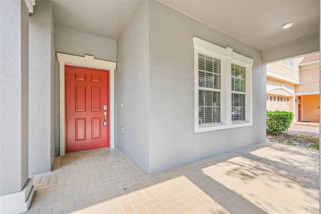 A covered front porch features a red door and a large window on a gray house — 13272 PENSHURST LANE, WINDERMERE, FL